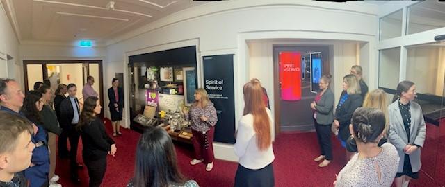 Photo of exhibition entrance with a number of people gathered while Lina Ranieri, APS Exhibition Lead introduces APS Academy staff to the exhibit.