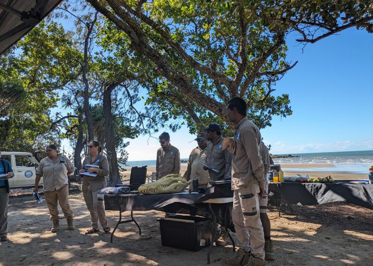 Image of eight people standing outside on Larrikia country around a table at the First Nations Land and Water Management Forum