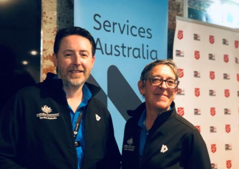 Photo in front of pull up banner of two people - CPSOs Nick and Rosemary - at the Community Partnership Pilot at Project 614, Salvation Army in Melbourne.