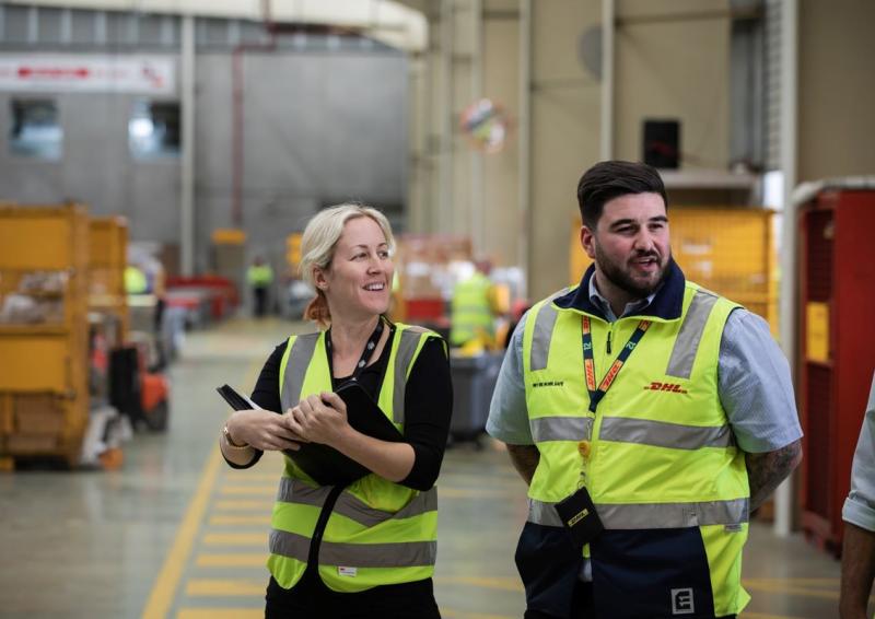 A photo featuring two people standing inside an industrial warehouse. 