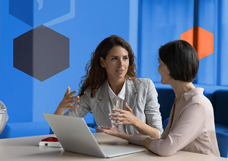 Two people sitting and conversing in front of an open laptop