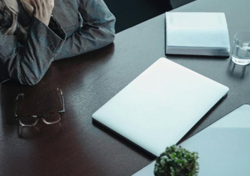 Image of person sitting a desk with a closed laptop, glasses resting on the desk and an open diary