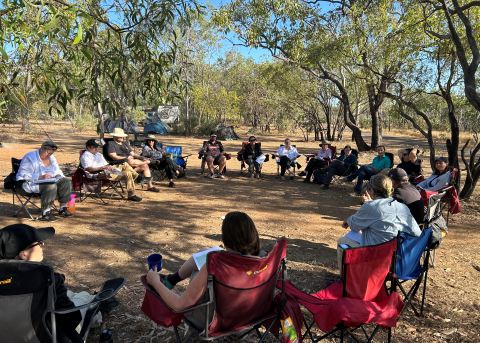 Photo of people sitting around on camp chairs in a circle in a open bushland setting.