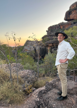 A photo of a male standing on a rocky outcrop with Australian rockscape behind him.