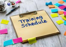 Picture of a clipboard with the words "Training Schedule" written on it, with post-it notes scattered around the clipboard