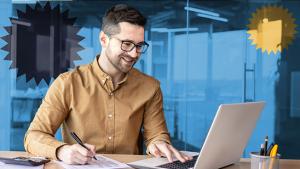 Person sitting at a desk working on a laptop and writing on a piece of paper