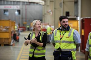 A photo featuring two people standing inside an industrial warehouse. 